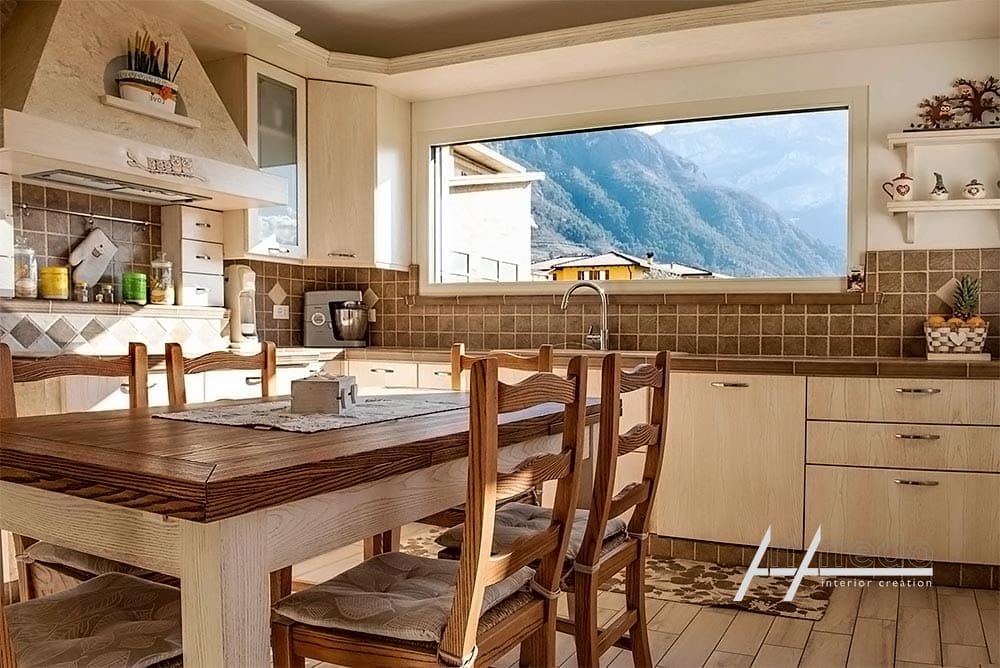 Interno della cucina moderna Cucine su Misura con tavolo da pranzo, sedie e armadietti in legno, dotato di un'ampia finestra con vista sul paesaggio montuoso. realizzata da ArtArredo snc di Piacenza.